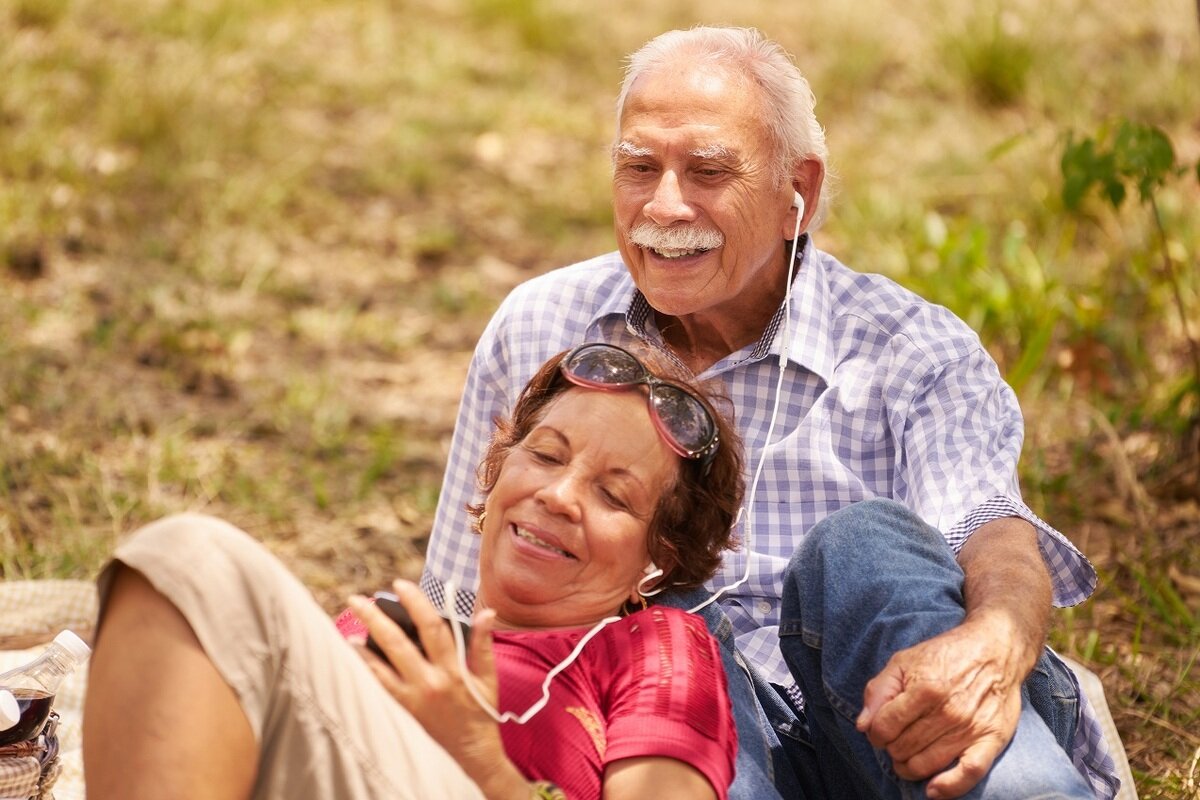 An older man and woman sitting on the grass, while smiling