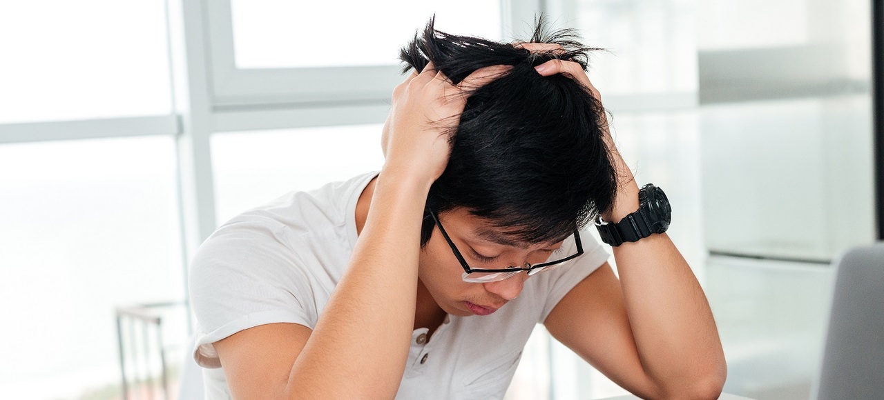 young Asian man sitting at a desk,holding his head